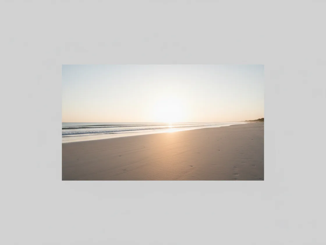 A wide empty beach at sunrise with smooth undisturbed sand and no people anywhere in the frame.