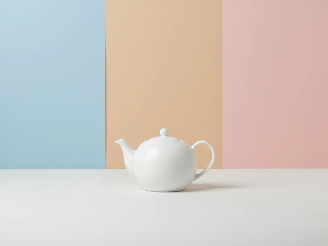 A white teapot photographed against a backdrop split into three different solid colors.